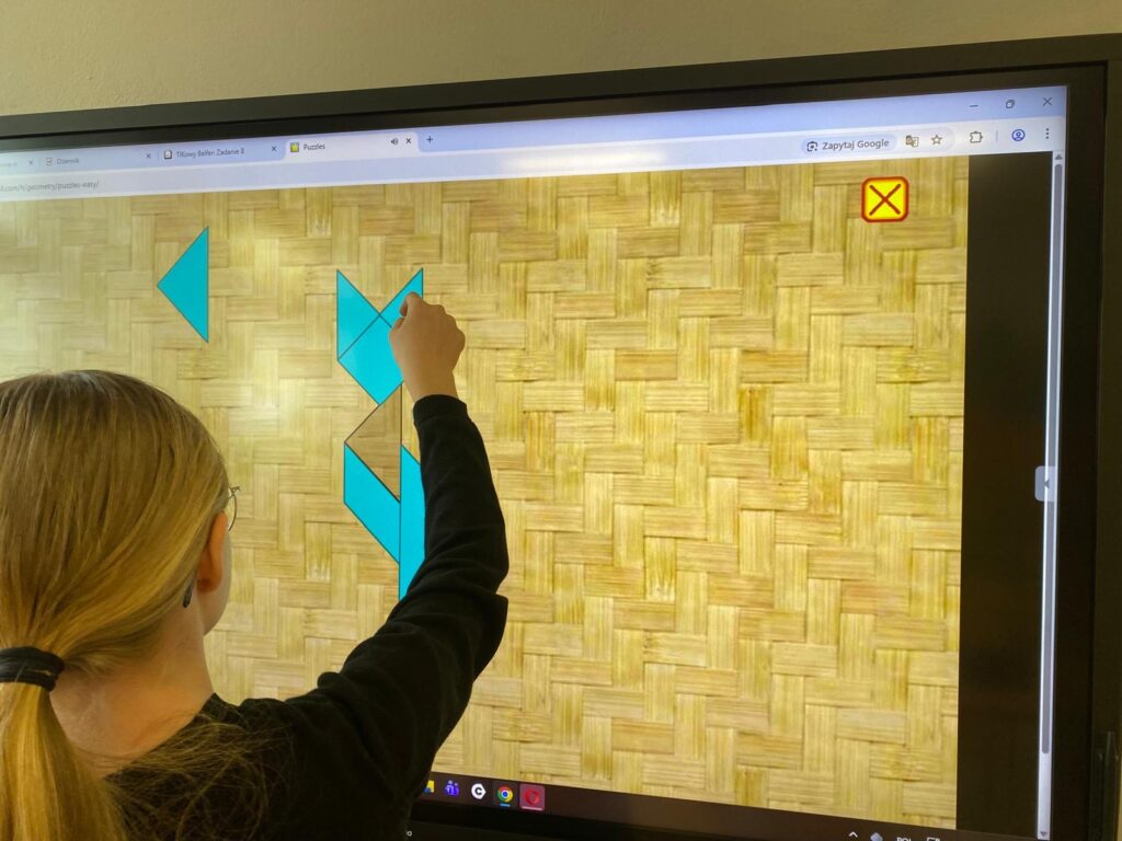 Na zdjęciu uczeń układający tangram na tablicy multimedialnej